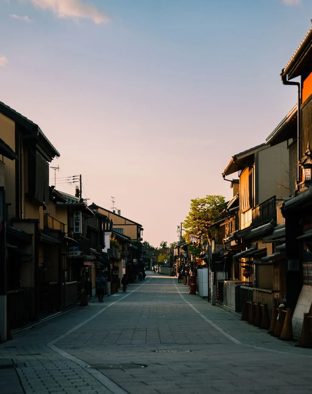 An empty Kyoto street of old wooden townhouses at dusk under a pink sky