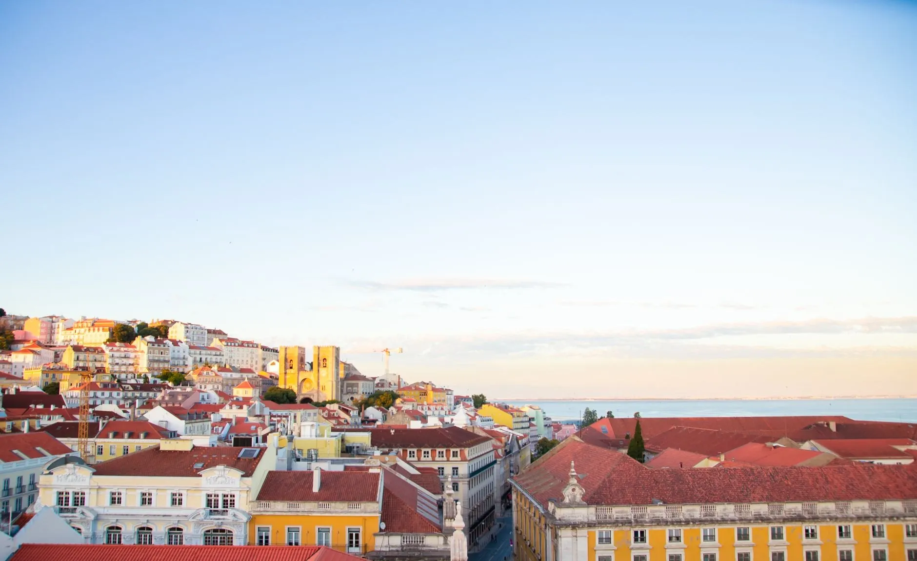 Lisbon's red rooftops and yellow arcades running down to the river under a pale morning sky