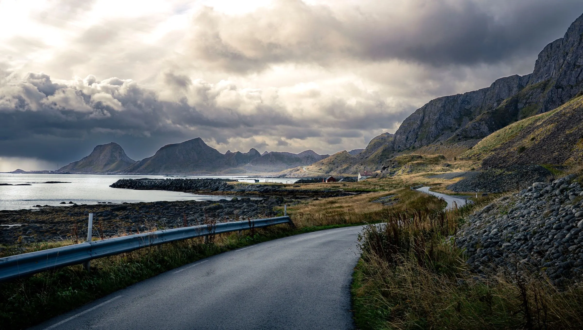 A narrow road winding along a rocky Arctic shore beneath dark mountains and heavy cloud