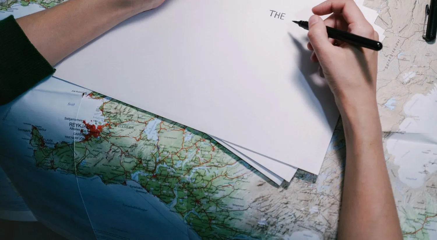 Hands writing on a sheet of paper laid over a road map