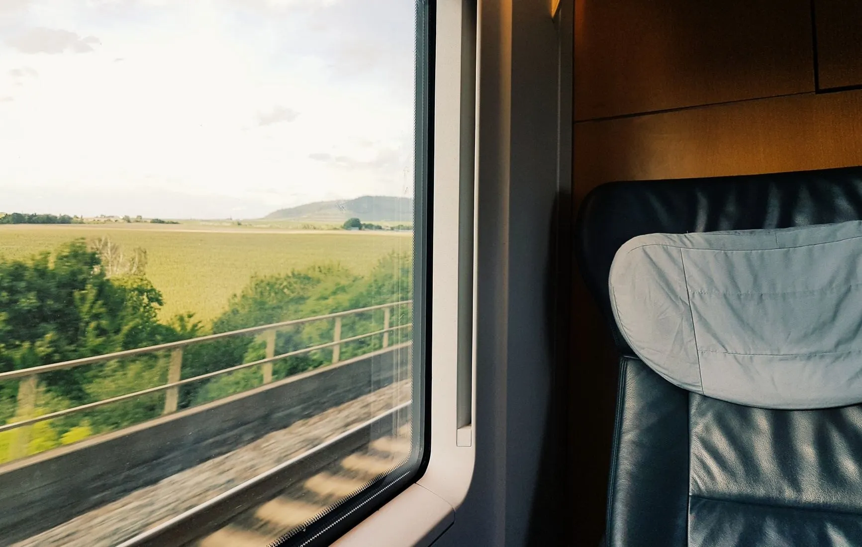 The view from a train seat through a large window onto green fields and low hills