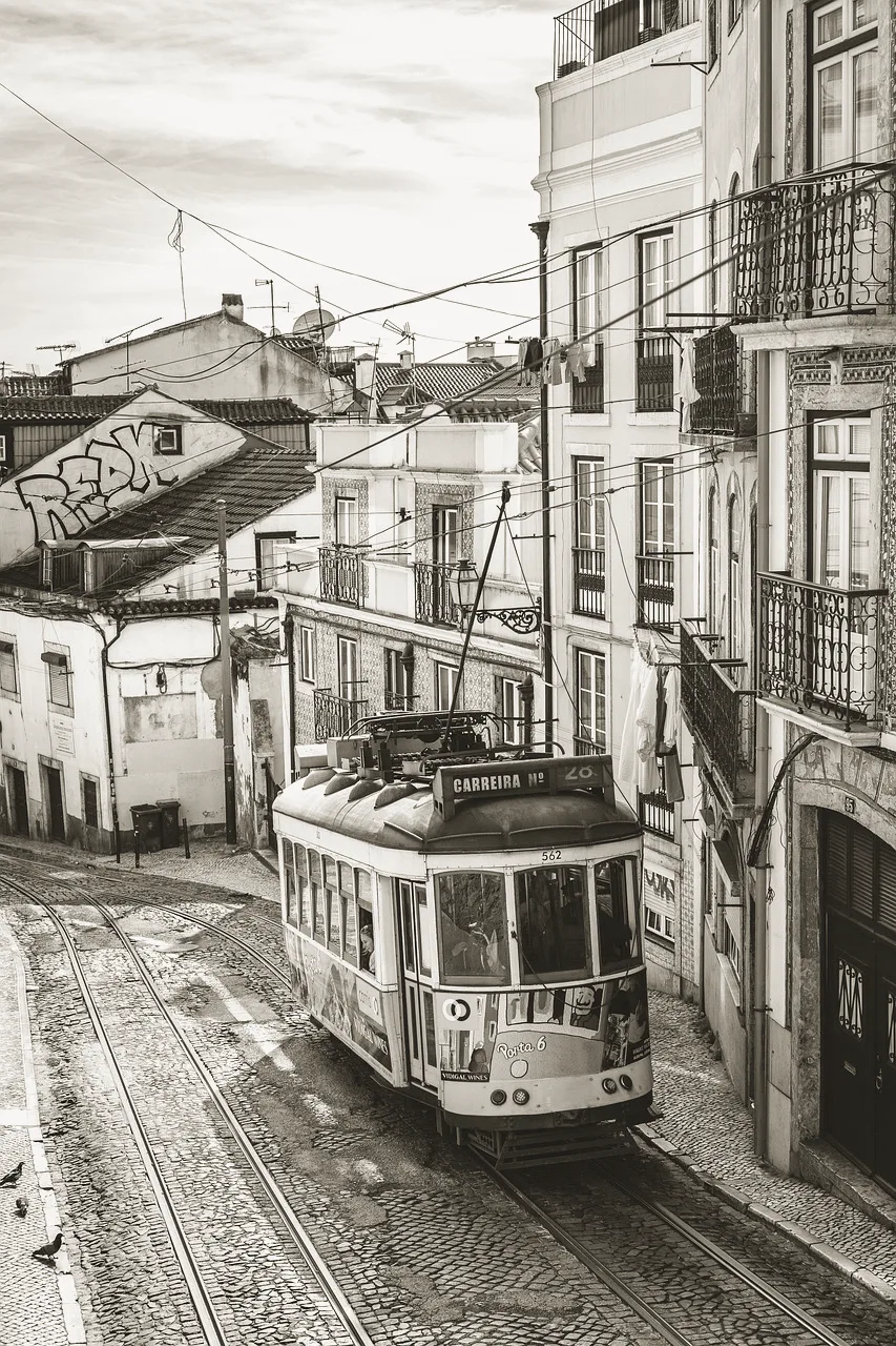 A route 28 tram coming down a steep cobbled Lisbon street between tiled facades and iron balconies